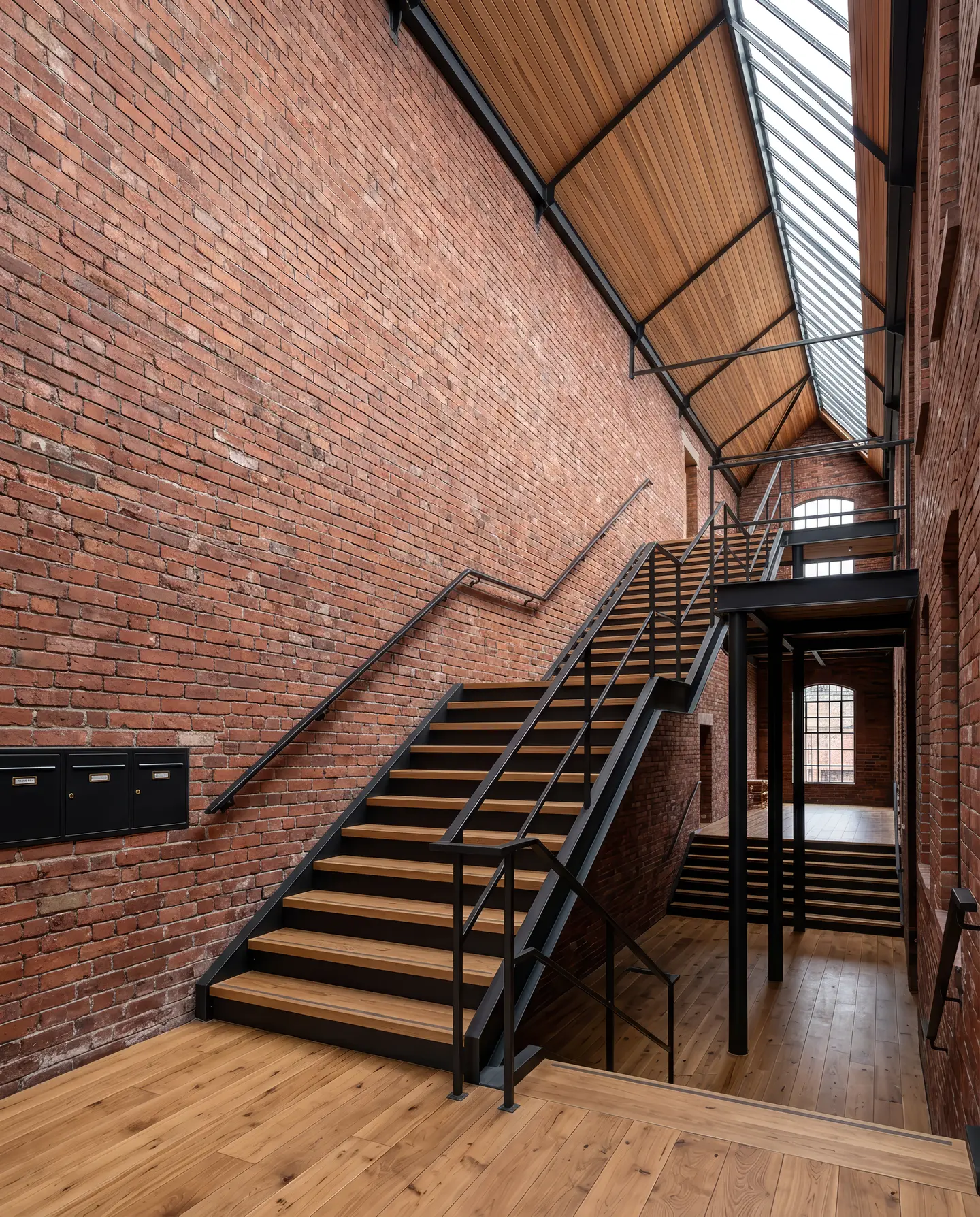 Het gemeenschappelijke trappenhuis met een stalen en eiken trap langs een bakstenen muur onder een shedlichtstraat
